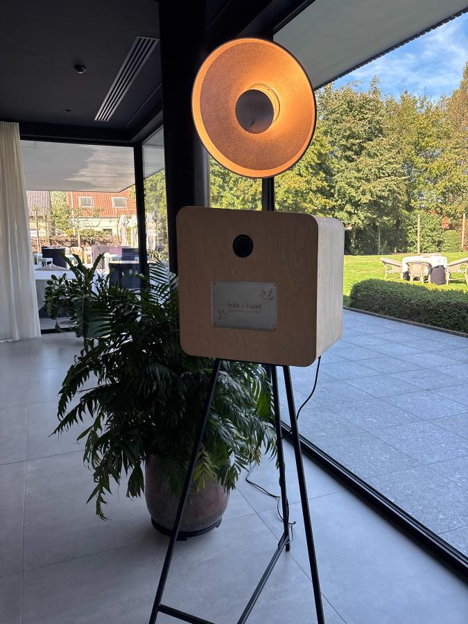 De booth met de gouden lamp naast een plant, voor een glazen gevel met een tuin erachter